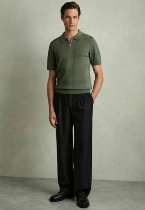 Cămașă polo verde cu dungi, cu mâneci scurte, având guler cu fermoar. Asortată cu pantaloni negri cu talie înaltă și pantofi negri.