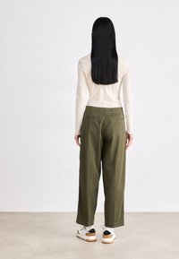 Grønne vide bukser laget av et glatt stoff. Stylet med en beige langermet topp. Hvite joggesko med svarte detaljer fullfører antrekket.