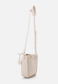 Bucketväska i slät beige läder med guldfärgade detaljer, justerbar axelrem och dragsnöre. Har en rund tagg på sidan.