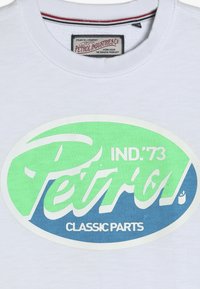 T-shirt in cotone bianco con una grande grafica ovale verde e blu con la scritta "Petrol IND.'73" e "CLASSIC PARTS". Collo arrotondato, maniche corte.