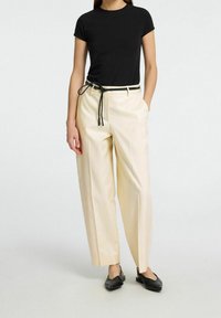 Beige vida byxor med svart dragsko, kombinerat med en åtsittande svart t-shirt. Materialet verkar slätt; byxorna har en avslappnad passform.