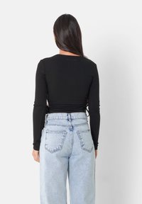 Svart ribbad långärmad topp med rundad halsringning, med justerbara snören vid midjan. Matchad med ljusblå högmidjade jeans.