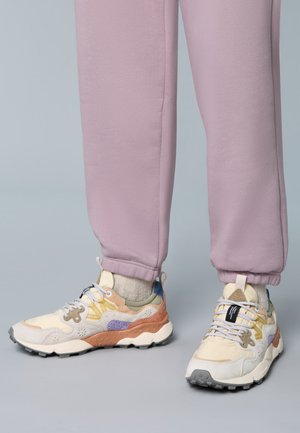 Multicolored sneakers with beige, brown, and purple accents, textured materials, and grey rubber soles. Paired with light purple joggers.