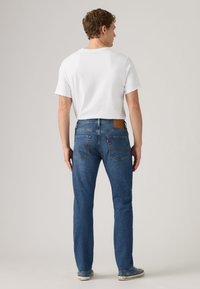 Blue denim jeans with a straight cut, back pocket detailing, and a brown leather brand patch. Accompanied by a plain white t-shirt.