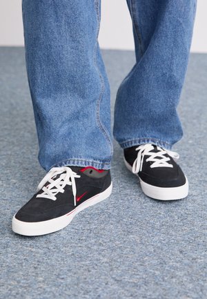 Fekete sportcipők piros részletekkel és fehér fűzőkkel. Alacsony szárú dizájn sima felülettel, kék farmernadrággal párosítva.