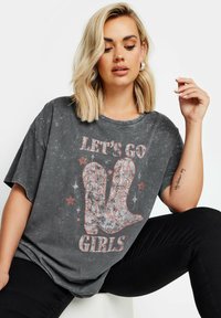 Harmaa, ylisuurikokoinen t-paita, jossa on kulunut pinta. Paidassa on teksti "LET'S GO GIRLS" ja graafinen kuva cowboy-kengistä koristeellisilla yksityiskohdilla.