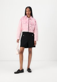 Rinnatud roosa denim jakk kahe esipocketiga, mustad tekstureeritud lühikesed püksid, mustad loafersid ja väike roosa käekott.