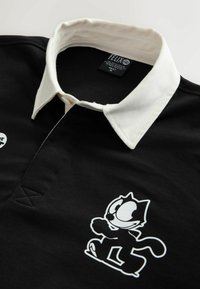 Schwarzes Poloshirt mit einem weißen Kragen, auf der linken Seite mit einem Felix der Kater-Graphic und strukturiertem Stoff. Markenetikett innen am Kragen sichtbar.