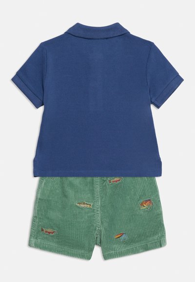 Πλάτη παιδικού μπλε μπλουζάκι πόλο με κοντά μανίκια και πράσινα βελουτέ σορτς με κεντητά σχέδια ψαριών και ομπρέλας.