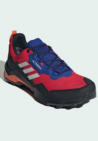 Punainen ja sininen urheilukenkä mustilla yksityiskohdilla, teksturoitua kangasta, kolme valkoista raitaa ja oranssi vetonauha. Kestävä ulkopohja, joka on suunniteltu pitoon.