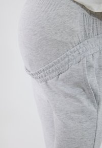 Hellgraue Jogginghose mit weicher Textur, elastischem Bund, Seitentaschen und gerafften Akzenten an den Hüften.