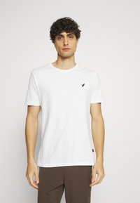 Tricou alb din bumbac, cu mâneci scurte și decolteu rotund. Previne un mic logo negru pe pieptul stâng. Croială dreaptă, ajustare lejeră.