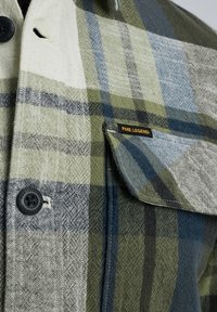 Chemise à col boutonné en tartan, présentant des couleurs vertes, bleues et blanches. Tissu texturé avec une poche poitrine et une étiquette "PME Legend".