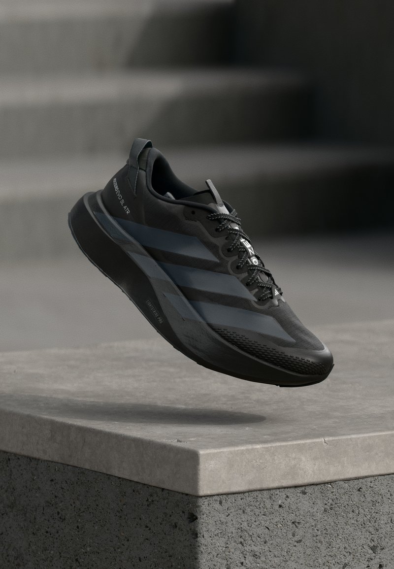 Tênis de corrida preto leve com design elegante, parte superior texturizada, sistema de amarração proeminente e detalhes refletivos, exibido em meio ao ar.