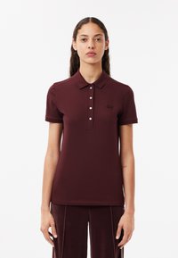 Polo di colore bordeaux con colletto, patta con cinque bottoni, maniche corte a coste e un piccolo logo ricamato sul petto.