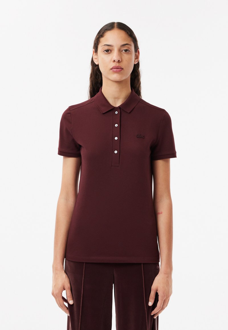 Polo di colore bordeaux con colletto, patta con cinque bottoni, maniche corte a coste e un piccolo logo ricamato sul petto.
