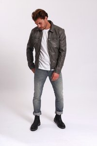 Grå läderjacka med två bröstfickor med dragkedja, krage, i kombination med en vit skjorta och ljusblå jeans. Svarta ankelstövlar.