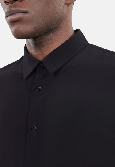 Sort skjorte med knapper, glat tekstur, struktureret krave og to synlige sorte knapper ved halsudskæringen. Simpelt og elegant design.