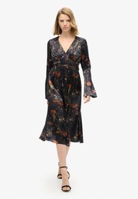 Vestido negro de flores con escote en V, cintura fruncida y mangas acampanadas. Presenta flores vibrantes y acentos dorados sobre una tela suave.