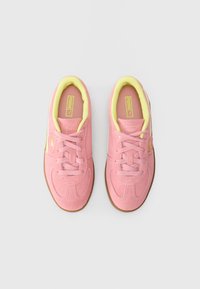 Et par rosa semskede sneakers med gule innvendige detaljer og brune såler, med Puma-merke på sidene og innersålene, vist ovenfra.