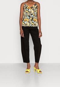 Blommig cami-top i svart, gult och grönt med tunna band, parat med säckiga svarta byxor och gula klacksandaler med en rosettdetalj.