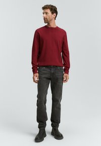 Rød langærmet sweater, medium fit, kombineret med slim-fit grå jeans. Sorte ankelstøvler fuldender outfittet. Simpelt design, ingen synlige mønstre.