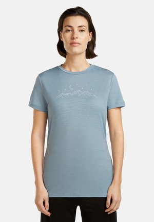Woman wearing a light blue t-shirt with a white line drawing of mountains, a crescent moon, and stars on the chest.