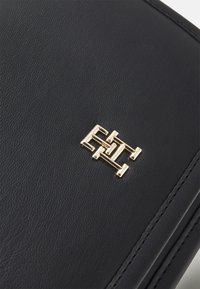 Prodotto in pelle nera con superficie testurizzata e un accento logo geometrico in tonalità oro nell'angolo. I bordi cuciti aggiungono dettaglio.