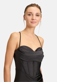 Czarna dopasowana sukienka na cienkich ramiączkach, z drapowanym dekoltem i usztywnioną górą. Gładka tekstura materiału z pionowymi szwami.