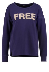Sudadera morada de corte relajado, con la palabra "FREE" en letras beige texturizadas en la parte frontal y aberturas laterales en el dobladillo.
