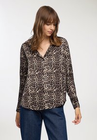 Bluzka w zebrze z gładkiego materiału; posiada kołnierzyk, długie rękawy i zapięcie na guziki z przodu. Luźny krój z zaokrąglonym dołem.