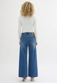 Wijdvallende blauwe denim jeans met een hoge taille, voorzien van een leren label aan de achterkant, twee achterzakken en een omgeslagen zoom.