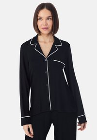 Haut de pyjama noir à manches longues avec un bord en satin blanc, doté d'un col et d'une poche avant, fabriqué en tissu doux et léger.