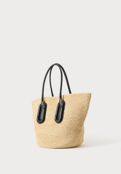 Sac cabas tissé beige avec des anses en cuir noir, présenté debout sur un fond clair uni.
