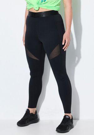 Leggings sportivi neri con inserti in rete sulle cosce, vita alta e design aderente. Abbinati a scarpe sportive nere.