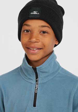 Black ribbed beanie with branded patch; light blue fleece shirt with a half-zip collar and contrasting black zipper detailing.
