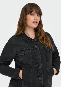 Svart denimjacka med klassisk design, som har två bröstfickor, knäppning med knappar och en något blekt yta.