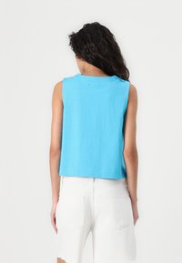 Light blue sleeveless top made of cotton, with a cropped design and a round neckline. The fabric has a smooth texture.