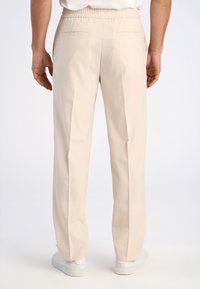 Beige Hose mit elastischem Bund, geradem Bein, zwei Gesäßtaschen und glatter Stofftextur, kombiniert mit weißen Turnschuhen.