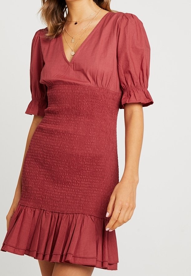 Robe bordeaux à manches bouffantes avec un corsage smocké et un ourlet à volants. Tissu léger, décolleté en V et texture lisse.