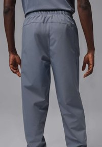 Szare spodnie sportowe z elastyczną talią, zwężanymi nogawkami oraz siateczkowymi panelami po bokach zapewniającymi wentylację. Gładka tekstura, minimalistyczny design.