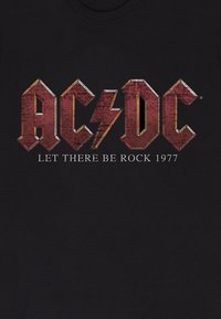 Černé bavlněné tričko s výrazným rezavě červeným logem "AC/DC" a designem blesku, s textem "NECHŤ BUDE ROCK 1977" v bílé barvě.