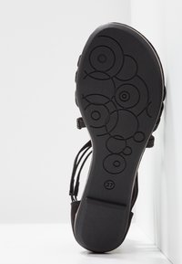 Semelle d'une sandale noire montrant des motifs circulaires et la taille 37 embossée au bas, présentée sur un fond blanc.