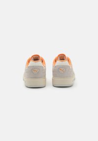 Une paire de baskets Puma en suède beige avec un intérieur orange, vue de dos sur un fond blanc.
