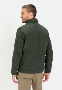 Mørkegrøn, quilted jakke med høj krave, lynlås foran og sidelommer. Har et struktureret mønster og elastiske manchetter for en god pasform.