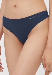 Marinblå Calvin Klein-stringtrosor i ett mjukt, stretchigt tyg; inkluderar en liten logotyp på midjebandet för varumärkesidentifiering.