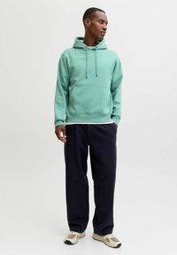 Mintgrüner Hoodie mit einer Fronttasche und Kordelzug, kombiniert mit marineblauen, weit geschnittenen Hosen und hellen Sneakers. Glatte Textur, lässiges Design.