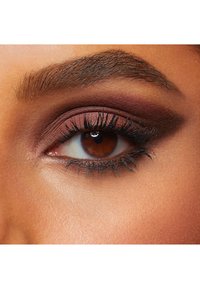 Gros plan d'un œil marron avec des cils sombres et épais. Les ombres à paupières présentent des nuances riches de bordeaux et de tons métalliques, avec un sourcil bien dessiné. Texture de peau lisse.