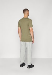 T-shirt de manga curta verde-azeitona com decote redondo, combinada com calças de fato jogger cinza-claro, com um corte descontraído e punhos elásticos.