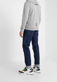 Sudadera de algodón gris con capucha y detalles en la parte trasera, combinada con jeans de mezclilla azul. El calzado presenta un diseño atlético colorido.